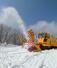 青空に向かって雪を勢いよく飛ばす除雪車＝３日、佐渡市の大佐渡スカイライン