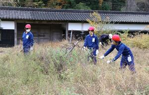 長屋門(後方)の周りの草を刈る児童ら=三条市月岡