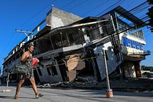 フィリピンのミンダナオ島で、地震により倒壊した建物のそばを通り過ぎる女性=9日、ジェネラルサントス(ロイター=共同)