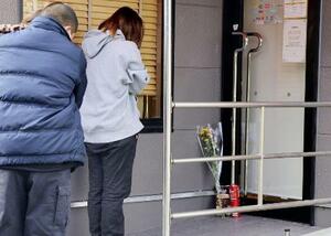 現場となった店舗の出入り口に献花し、手を合わせる人=昨年12月、北九州市小倉南区