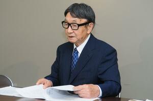 仮処分の申し立てについて説明する早津輝雄さん＝２５日、県庁