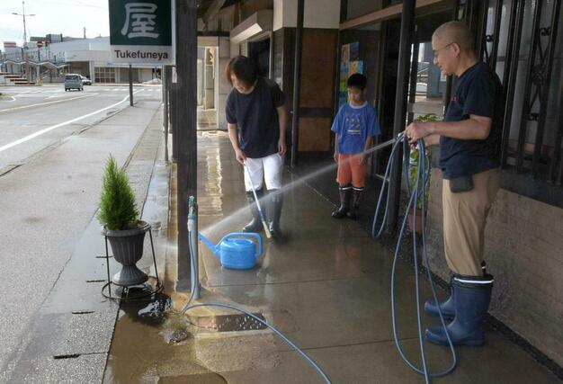 大雨で旅館に流入した水を掃き出しながら、付着した泥などを洗い流す住民=3日、上越市中央1の附船屋