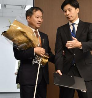 職員(右)の介助を受けながら初登庁した、パラ選手から初のスポーツ庁長官となった河合純一氏=1日午前、東京・霞が関