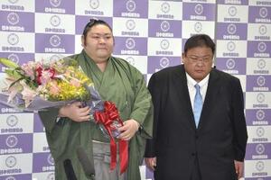 引退記者会見を終え花束を手にする元幕内剣翔。右は追手風親方=4月、東京・両国国技館