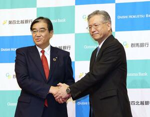 記者会見で握手をする第四北越フィナンシャルグループの殖栗道郎社長(右)と群馬銀行の深井彰彦頭取=24日、東京都内のホテル