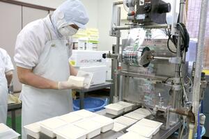 豆腐に欠けや割れがないか入念にチェックする職員の宇田貴弘さん＝佐渡市栗野江