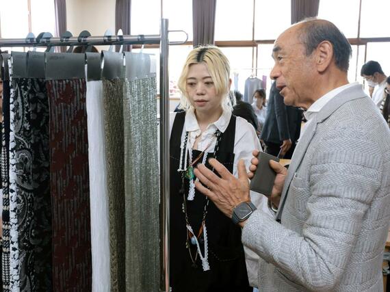 製品の説明を聞くニットアーティストの蓮沼千紘さん（左）＝５月１４日、五泉市