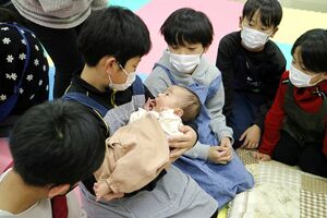 赤ちゃんを見つめる河原田小の児童たち。児童とふれ合った赤ちゃんは終始ご機嫌だった=佐渡市河原田本町