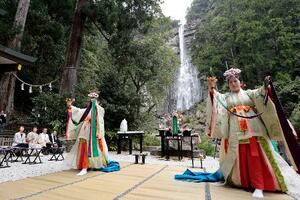 熊野那智大社の「桜花祭」で舞を披露する巫女。奥は那智の滝=14日午前、和歌山県那智勝浦町