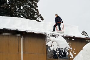 屋根の雪下ろしをする男性=2023年2月、長岡市