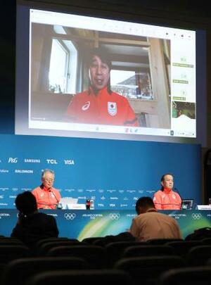 記者会見する日本選手団の伊東秀仁団長(左)ら。大型モニターはオンラインで出席した原田雅彦副団長=13日、イタリア・ミラノ(共同)