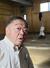 ２０２５年１２月、思い出を語る常盤山親方。後ろの稽古場の壁には師匠の元横綱初代若乃花の写真＝東京都板橋区の常盤山部屋