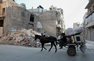 シリア北部アレッポで、破壊された建物のそばを通る家財道具を積んだ馬車=6月24日(ロイター=共同)
