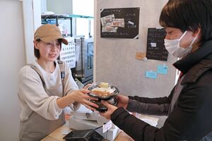 子ども食堂で、家族連れにカレーを手渡す桜井智子さん=柏崎市安田