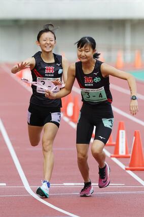 女子 新潟明訓の3区篠澤葉(左)が4区高山光帆にタスキをつなぐ=新潟市中央区