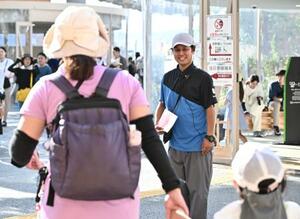 案内所前で来場者に笑顔で声をかける「ゲストサービスアテンダント」の村浩史さん=7月、大阪市此花区の夢洲