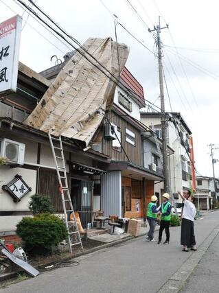 飛ばされたトタン屋根を調査し、状況を聞き取る気象庁機動調査班＝１１日、魚沼市小出島