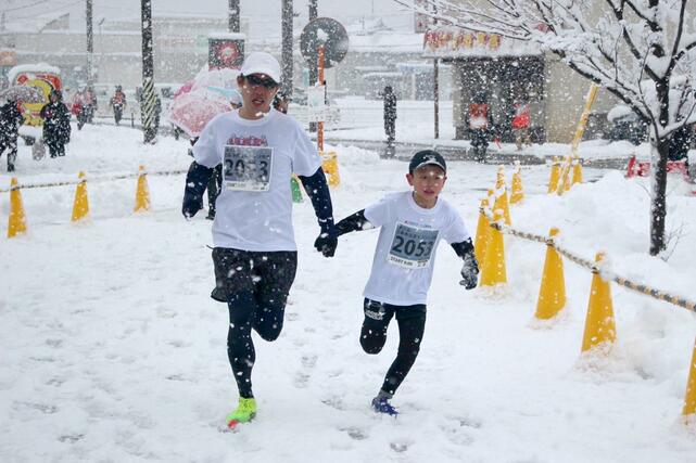 
雪が降る中、ゴール目前に手をつないで力強く走るランナー＝１月１日、三条市
