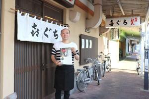 クラウドファンディングのチラシを持ち店の前に立つ店主の木口文敏さん=新潟市中央区古町通10
