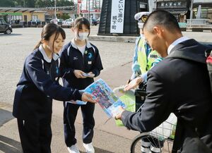 自転車利用者にチラシを配り、ヘルメット着用を呼びかける高校生たち=村上市田端町