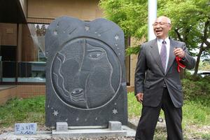 寄贈した石彫の前で笑顔を見せる彫刻家の佐藤賢太郎さん=阿賀町鹿瀬支所