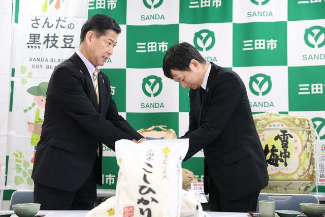 三田市産コシヒカリの試食後、三田市の田村克也市長（左）と握手を交わす上越市の中川幹太市長＝２９日、兵庫県三田市のＪＡ兵庫六甲三田支店