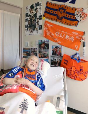 アルビグッズに囲まれたおぎの里の部屋で闘病生活を送る渡辺光子さん=新潟市秋葉区荻野町