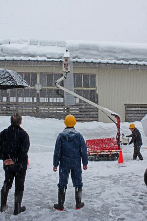 屋根雪下ろし機を視察する花角英世知事(左)=3月3日、三条市早水