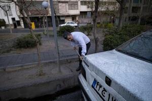 イランの石油施設が攻撃され、すすが付いた車を掃除する男性=3月8日、テヘラン(ゲッティ=共同)