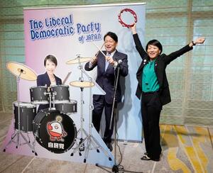 自民党大会の会場に設置された高市首相のフォトパネルの横でポーズをとる小野寺五典税調会長(左)と鈴木貴子広報本部長=12日午前、東京都内