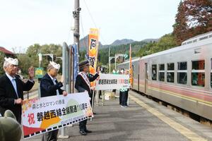 磐越西線全線開通110周年を祝い、横断幕を掲げて上り列車を迎える阿賀町の関係者ら=阿賀町の津川駅