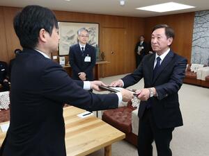 中川幹太市長から引き継ぎ書を受け取る小菅淳一さん(右)=6日、上越市役所