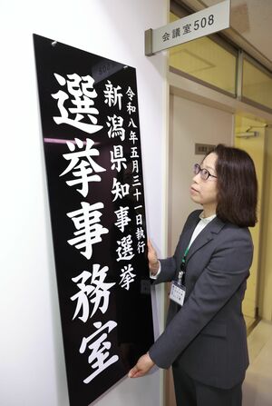 選挙事務室に看板をかける県選管の八幡己津子書記長＝１６日、県庁