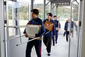 石川県輪島市の県立門前高で、完成した仮設校舎に勉強机や椅子を運び込む生徒たち=5日午前