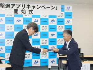 詐欺対策アプリのクーポンを手渡すトレンドマイクロ社の徳永信幸さん(右)=27日、県警本部