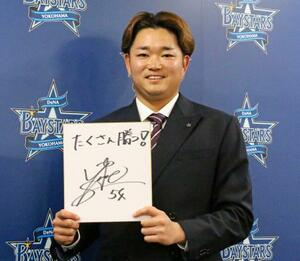 来期の抱負を書いた色紙を手にポーズをとるDeNAの石田裕=4日、横浜市の球団事務所