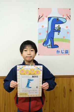 道の駅加治川の公式キャラクター「かじ豆」のポスターの前に立つ、加治川小の前田基成さん=新発田市上今泉