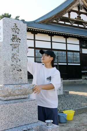 墓掃除の代行で墓石を拭き上げる学生=阿賀野市下条町