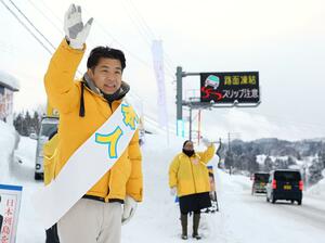 行き交う車一台一台に手を振る鷲尾英一郎さん＝９日、長岡市北荷頃