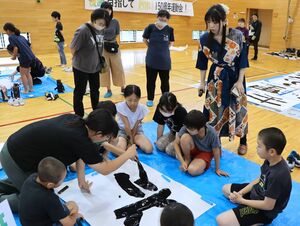 下田彩水さん(右から2人目)の指導で大書体験をする児童=糸魚川市の下早川小