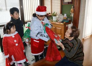 お年寄りにクリスマスプレゼントを手渡す小学生=12月22日、村上市早稲田