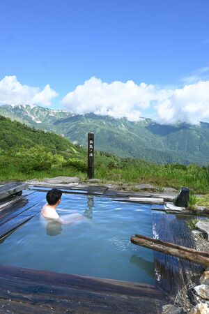 北アルプスの山並みを眺めながら湯に漬かる観光客=21日、糸魚川市の蓮華温泉