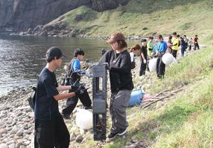 力を合わせ、大野亀付近の海岸に流れ着いたごみを運ぶ大学生=佐渡市
