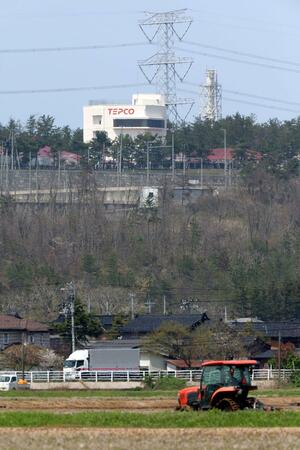 柏崎刈羽原発の鉄塔を背に田起こしを行う農家。7号機の燃料装塡が始まったこの日も、日常の風景が広がっていた=4月15日、刈羽村