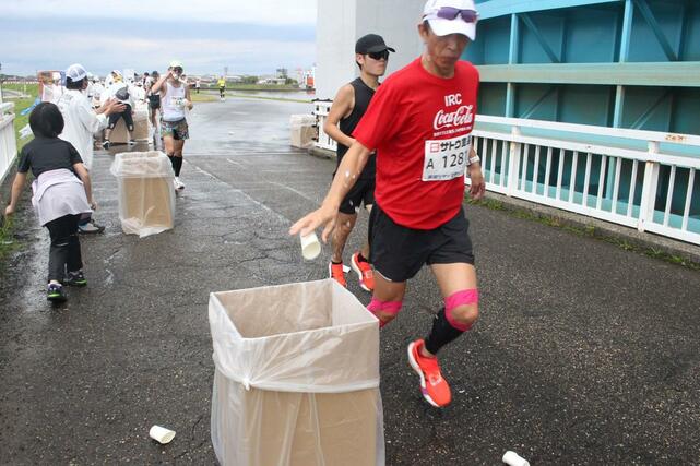 飲み終わった後、使用済みの紙コップをごみ箱に捨てるランナー＝12日、新潟市西区