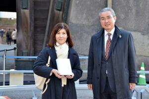 皇居・東御苑の4千万人目の入園者として宮内庁の古賀浩史管理部長(右)から記念品を受け取った山田裕美子さん=11日午後、東京都千代田区