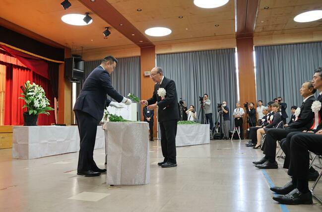 花を手にし献花台へ向かう式典実行委員長の中野洸さん=13日、佐渡市