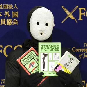 記者会見で著書を手にする覆面作家の雨穴さん=2025年1月、東京都千代田区の日本外国特派員協会