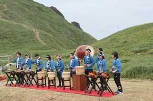 トビシマカンゾウを背に、芸能を披露する住民ら=6月9日、佐渡市願