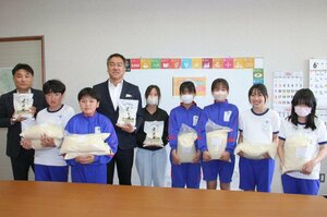 ロッテホテルアライの福井朋也社長(左から4人目)から贈られたコメ袋を抱える児童=新井小